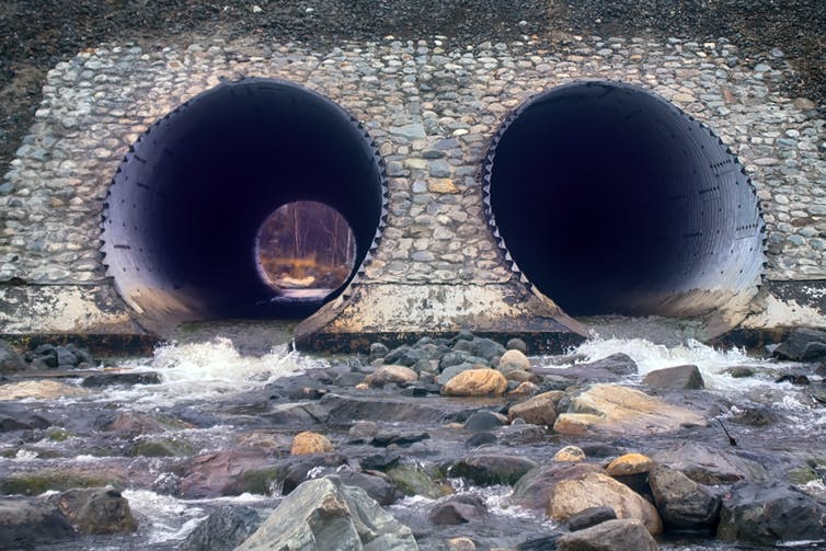  Два больших металлических туннеля с проточной водой, расположенные сбоку. насыпи автомагистрали. 